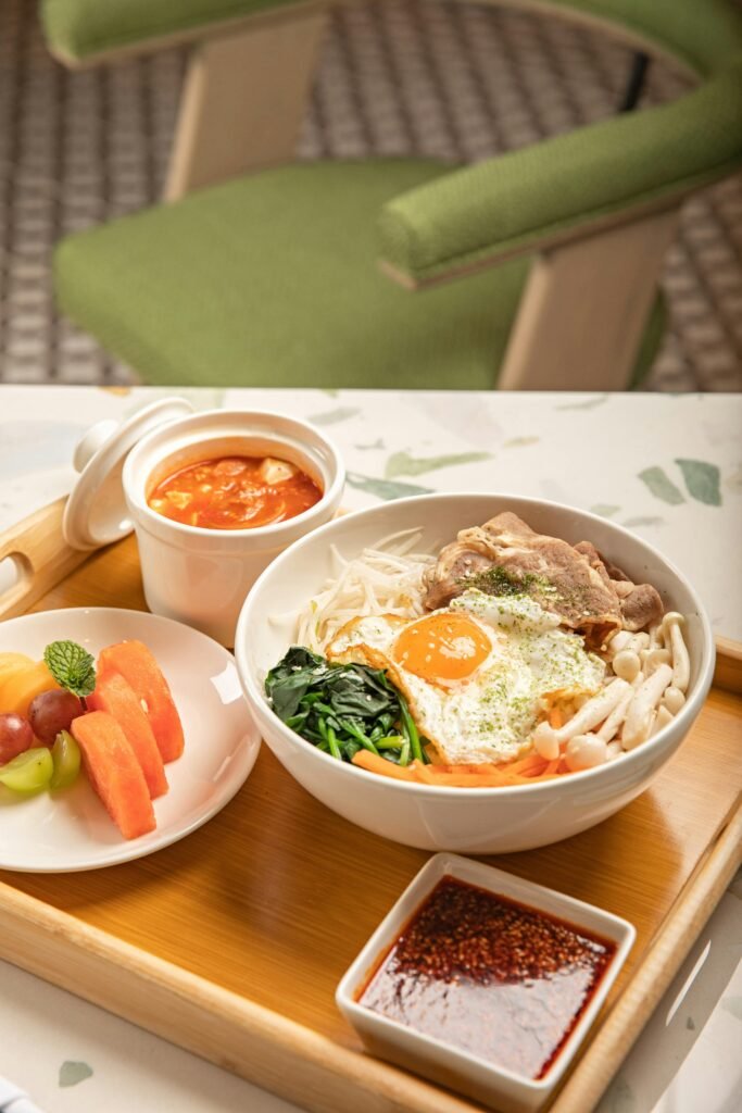 Korean Bibimbap with fresh vegetables, egg, and sauce on a table setting.